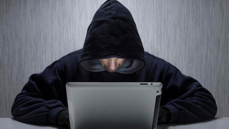 Wales, Monmouthshire, Monmouth. An anonymous hooded male using a tablet computer to represent a cyber criminal.